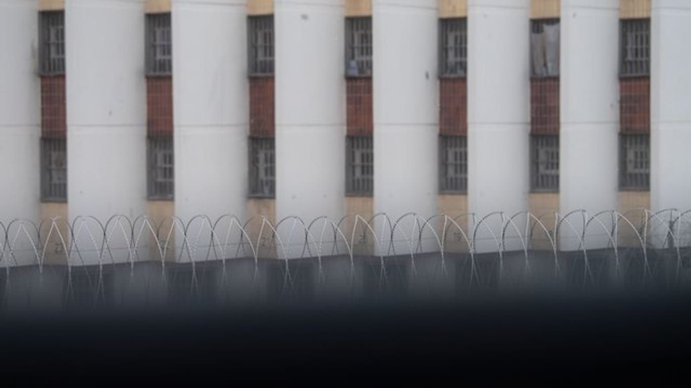 Stacheldraht liegt auf einer Gefängnismauer, im Hintergrund sind Zellenfenster der JVA Stuttgart-Stammheim zu sehen.