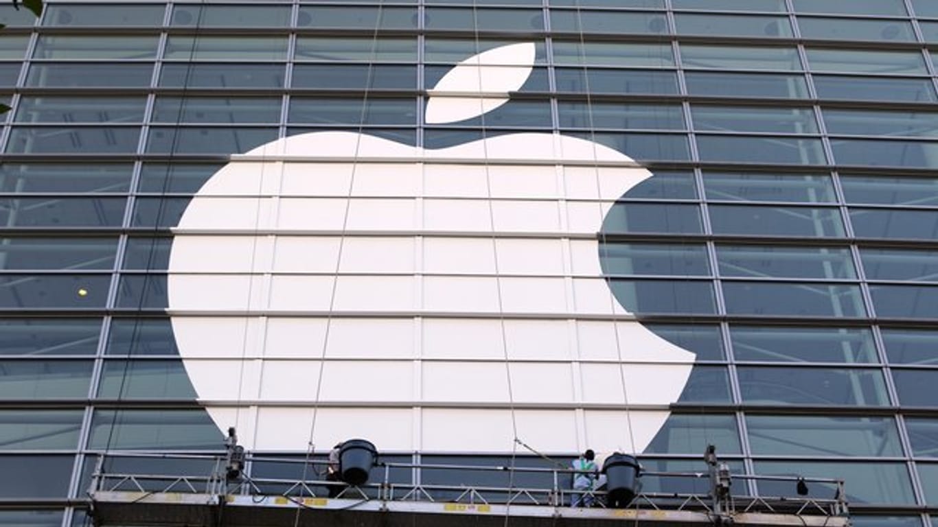 Arbeiter bringen ein übergroßes Apple-Logo an einer Glasfassade an.