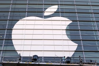 Arbeiter bringen ein übergroßes Apple-Logo an einer Glasfassade an.
