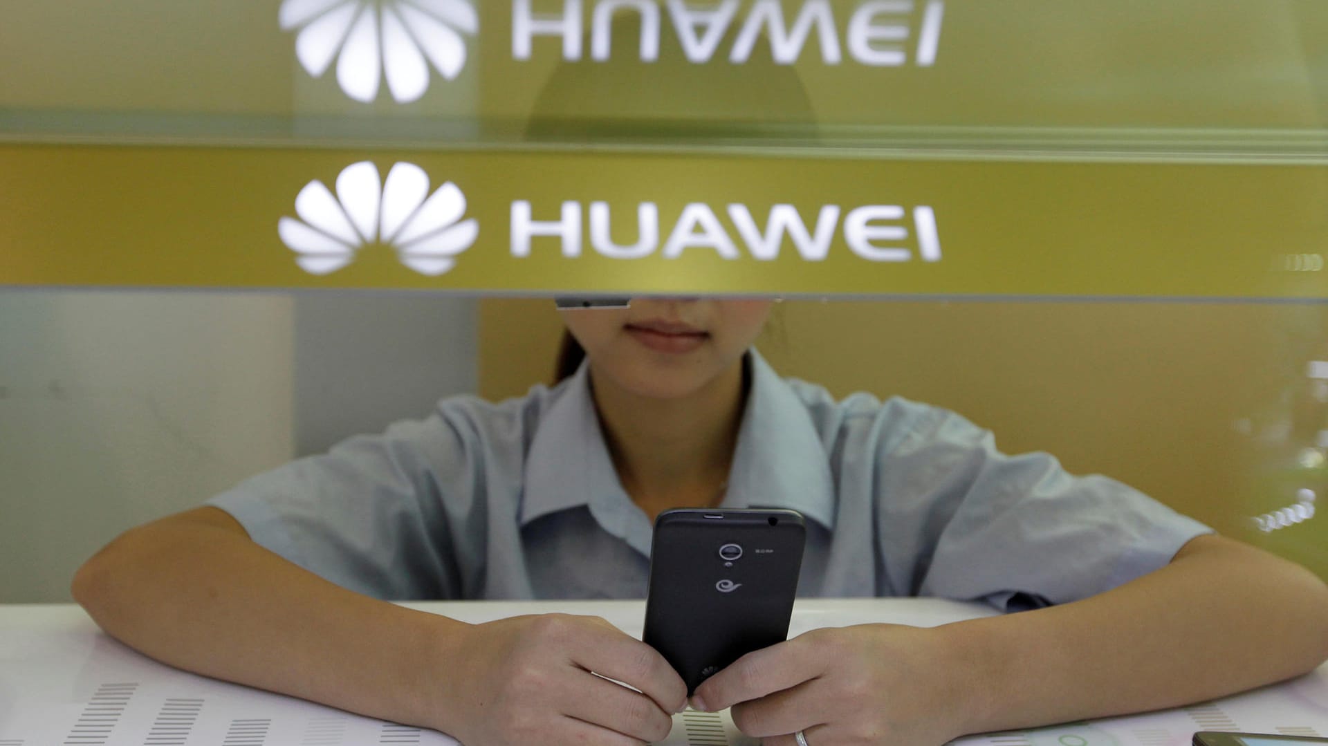 Eine Verkäuferin unter einem Huawei-Logo schaut auf ihr Smartphone: Der chinesische Smartphone-Hersteller und Apple sind Konkurrenten. (Archivbild)