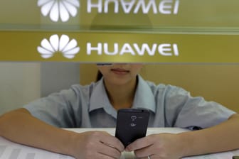 Eine Verkäuferin unter einem Huawei-Logo schaut auf ihr Smartphone: Der chinesische Smartphone-Hersteller und Apple sind Konkurrenten. (Archivbild)