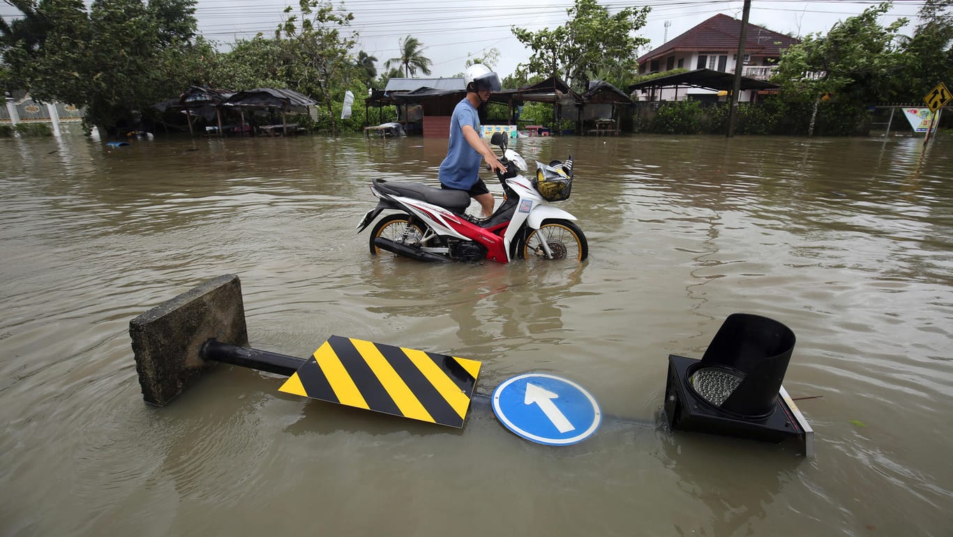 Nakhon Si Thammarat, Thailand: Ein Mann schiebt ein Motorrad über eine geflutete Straße. Die Schäden durch "Pabuk" halten sich in Grenzen.