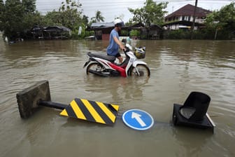 Nakhon Si Thammarat, Thailand: Ein Mann schiebt ein Motorrad über eine geflutete Straße. Die Schäden durch "Pabuk" halten sich in Grenzen.