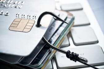 Ein Angelgaken in einer Bankkarte (Symbolbild): Mithilfe von Phishing-Mails versuchen Kriminelle, an sensible Daten von Bankkunden zu kommen.