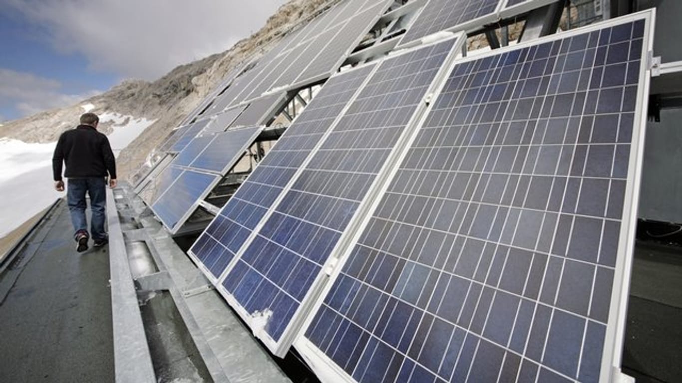 Ein Mitarbeiter der Umweltforschungsstation Schneefernerhaus auf der Zugspitze steht vor einer Solaranlage auf dem Dach des Gebäudes.