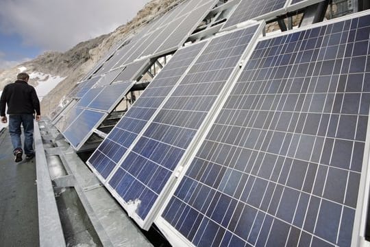 Ein Mitarbeiter der Umweltforschungsstation Schneefernerhaus auf der Zugspitze steht vor einer Solaranlage auf dem Dach des Gebäudes.