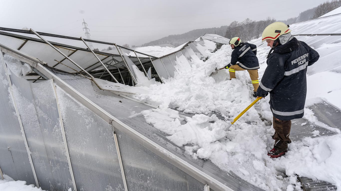 Salzburg in Österreich: Feuerwehrmänner schippen Schnee von einem eingebrochenen Gewächshausdach.