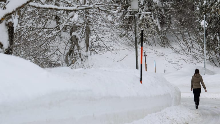 Bayern, Spitzingsee: Eine Frau geht auf einer Staße neben der Schneekante entlang.
