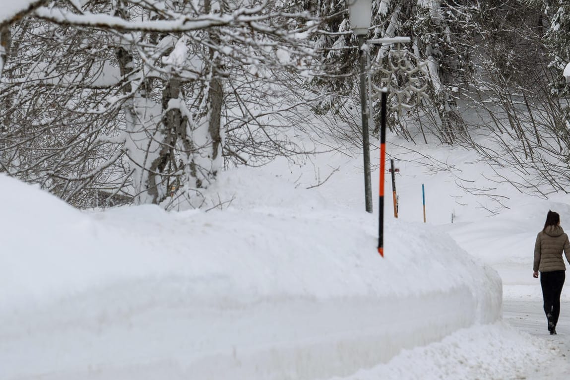 Bayern, Spitzingsee: Eine Frau geht auf einer Staße neben der Schneekante entlang.