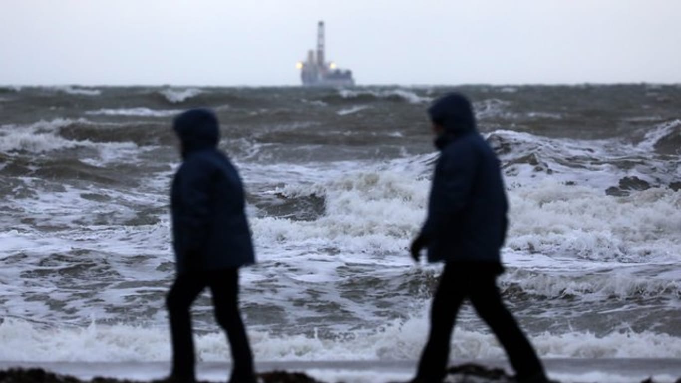 Spaziergänger sind in Warnemünde an der aufgewühlten Ostsee unterwegs.