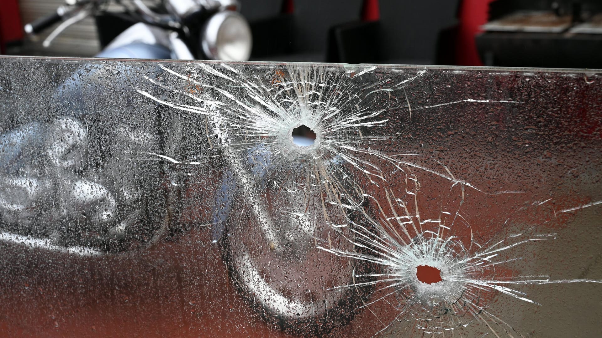 Einschusslöcher in einer Glasscheibe vor einer Spielhalle im Kölner Stadtteil Buchheim – vor dem Gebäude steht ein Motorrad: Rivalisierende Rockerbanden sollen für die wiederholten Schüsse verantwortlich sein. Einschusslöcher in einer Glasscheibe vor einer Spielhalle im Kölner Stadtteil Buchheim – vor dem Gebäude steht ein Motorrad: Rivalisierende Rockerbanden sollen für die wiederholten Schüsse verantwortlich sein.