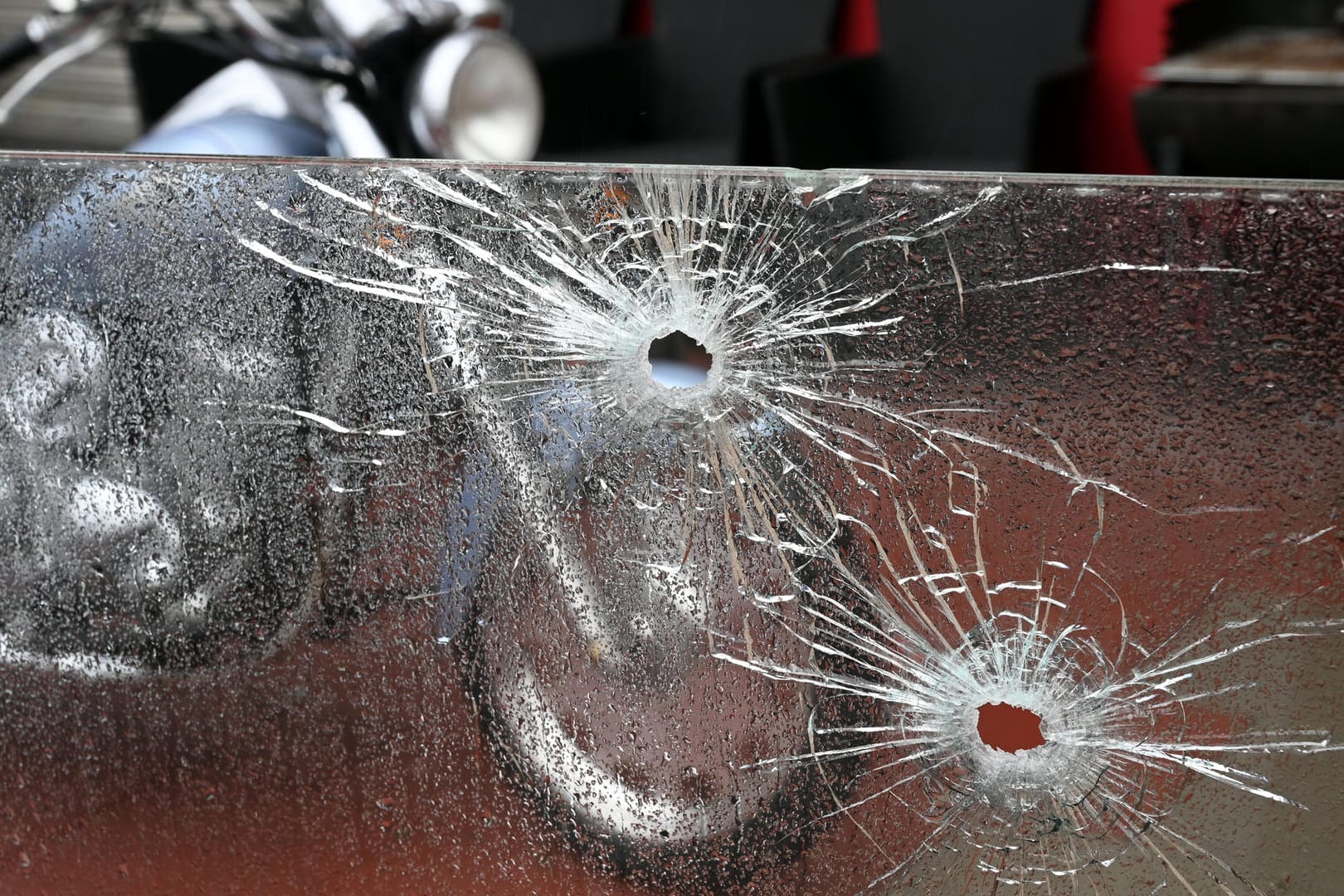 Einschusslöcher in einer Glasscheibe vor einer Spielhalle im Kölner Stadtteil Buchheim – vor dem Gebäude steht ein Motorrad: Rivalisierende Rockerbanden sollen für die wiederholten Schüsse verantwortlich sein.