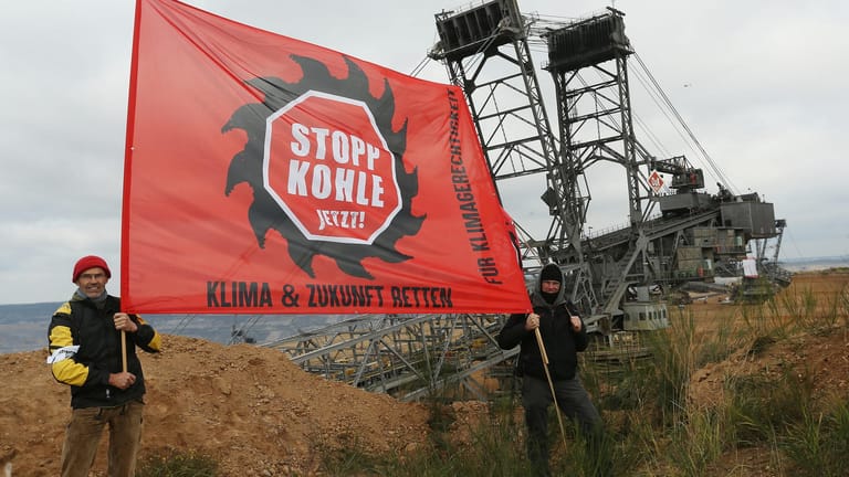 Aktivisten am Hambacher Tagebau: Sie halten einen Banner mit der Aufschrift "Stopp Kohle Jetzt! Klima und Zukunft retten". Im Hintergrund ist der Braunkohlebagger bereits gestoppt worden.