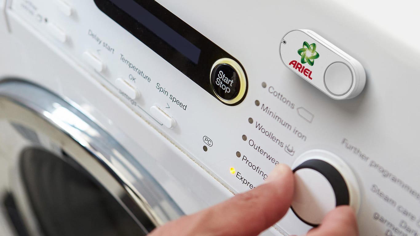 Das Foto zeigt einen Amazon Dash Button für die Marke Ariel, der an einer Waschmaschine klebt: Per Knopfdruck lässt sich beispielsweise neues Waschmittel bestellt.