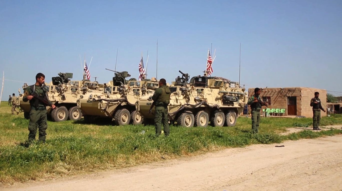 Kurdische Kämpfer bewachen in Nordsyrien amerikanische Militärfahrzeuge.