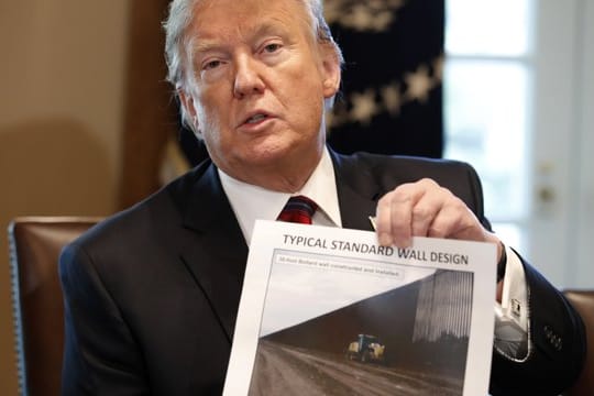 Donald Trump hält ein Foto einer möglichen Grenzmauer in der Hand.