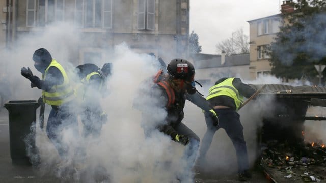 Teilnehmer einer Demonstration der "Gelbwesten" gehen in Bourges hinter ihren Barrikaden in Deckung, als Polizisten Tränengas einsetzen. Teilnehmer einer Demonstration der "Gelbwesten" gehen in Bourges hinter ihren Barrikaden in Deckung, als Polizisten Tränengas einsetzen.