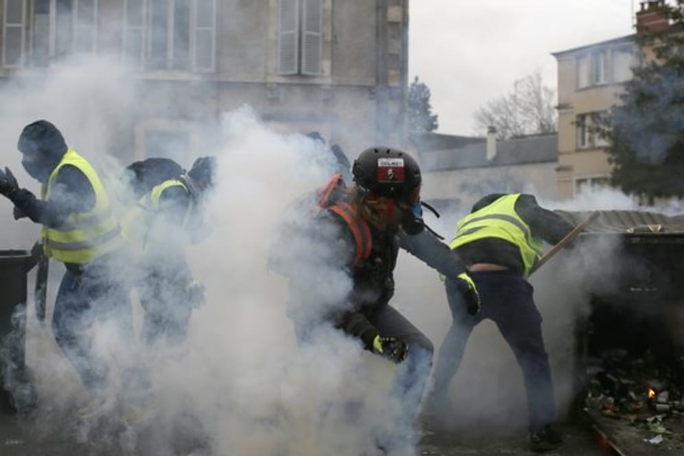 Teilnehmer einer Demonstration der "Gelbwesten" gehen in Bourges hinter ihren Barrikaden in Deckung, als Polizisten Tränengas einsetzen.