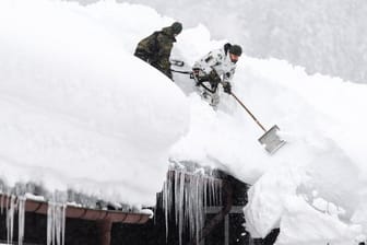 Einsatzkräfte der Bundeswehr befreien das Dach eines Wohnhauses von Schneemassen.