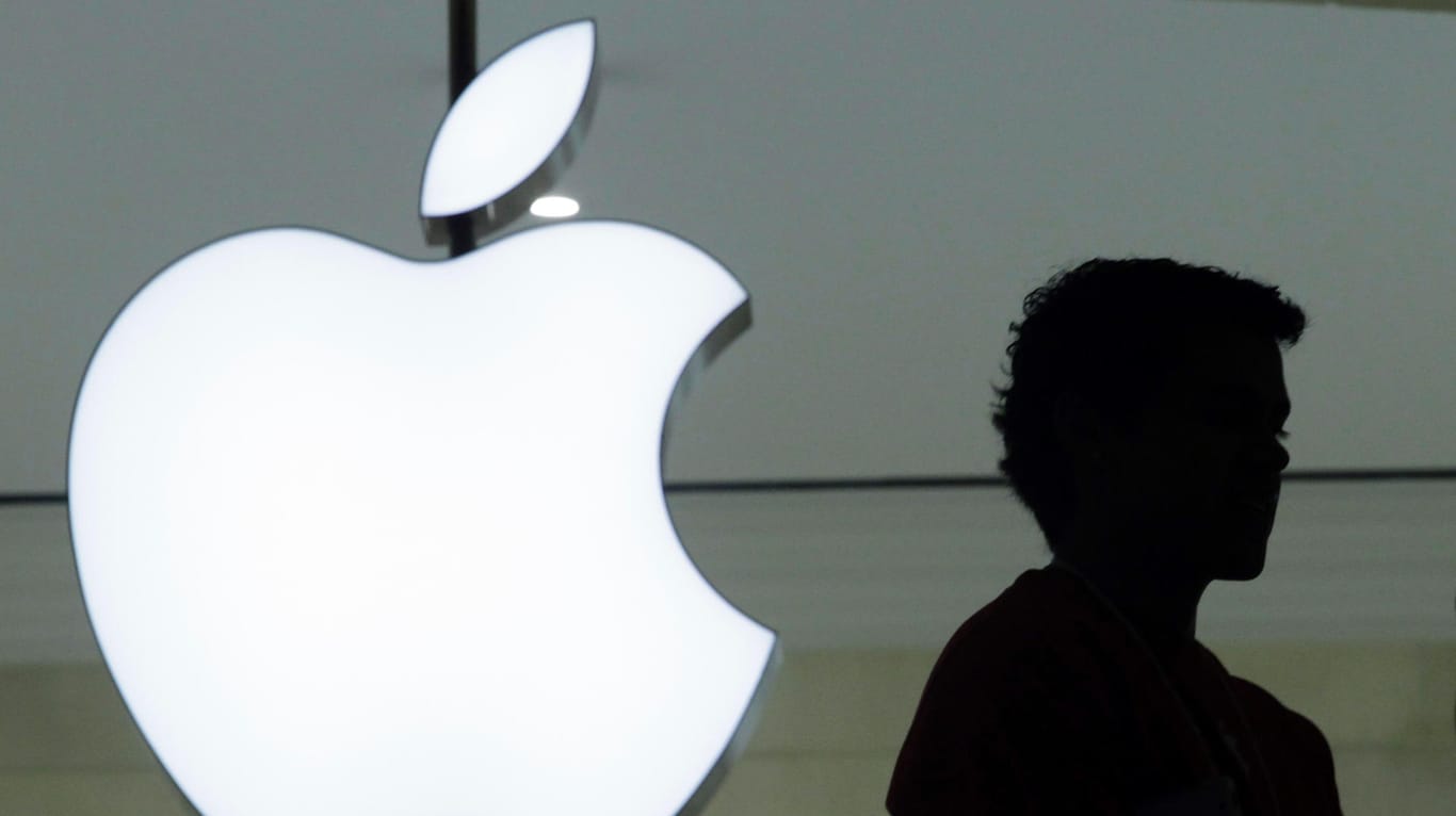 Ein Mensch vor einem Logo von Apple: Apple plant, weniger Neueinstellungen vorzunehmen.