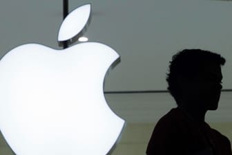 Ein Mensch vor einem Logo von Apple: Apple plant, weniger Neueinstellungen vorzunehmen.