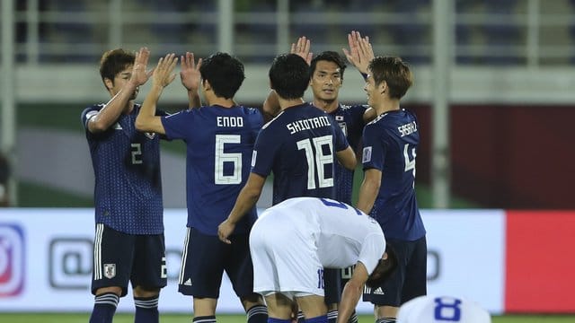 Japans Spieler (hinten) feiern den Sieg über Usbekistan.