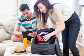 Frau packt einen Koffer: Urlaubsreisen nur mit Handgepäck sind eine Herausforderung – es kommt darauf an, klug zu packen.