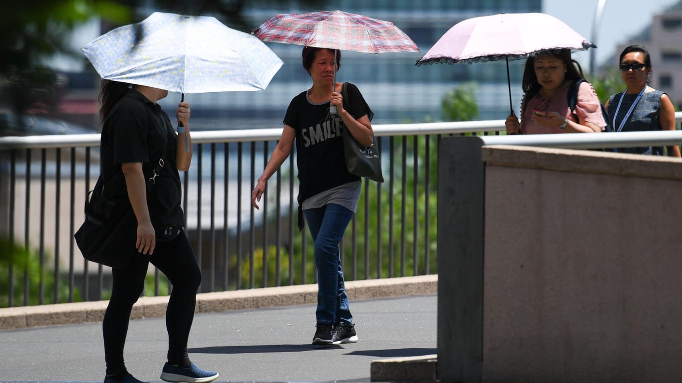 Fußgänger schützen sich mit Schirmen vor der Sonne: Die andauernde Hitze lässt sogar den Asphalt schmelzen.