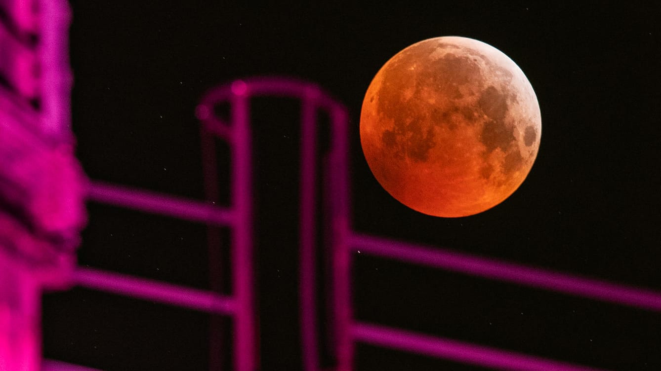 Duisburg: Als roter, sogenannter "Blutmond" präsentiert sich der Vollmond neben einem angestrahlten Hochofen im Landschaftspark Duisburg, während er in den Kernschatten der von der Sonne angestrahlten Erde tritt.