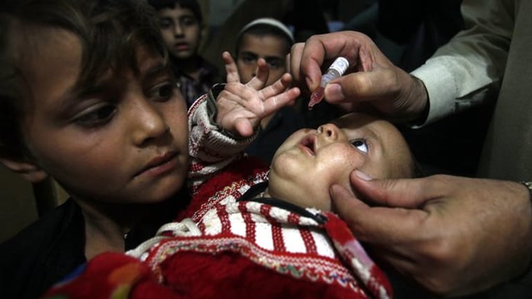 Ein pakistanischer Helfer impft ein Kind mit Tropfen.