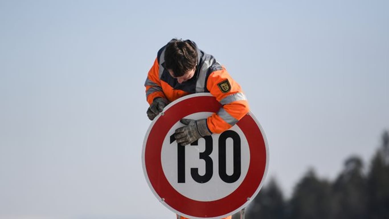 Ein Straßenwärter montiert an einer Autobahn ein Schild zur Geschwindigkeitsbegrenzung.