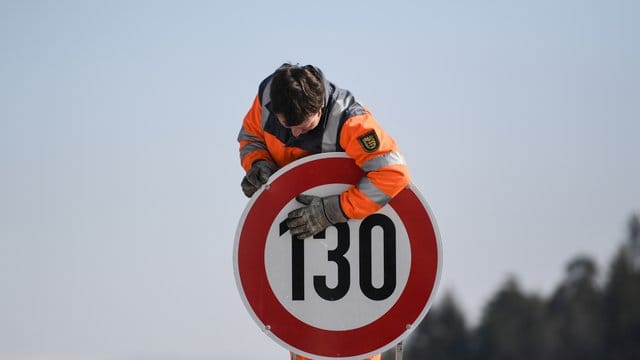 Ein Straßenwärter montiert an einer Autobahn ein Schild zur Geschwindigkeitsbegrenzung.