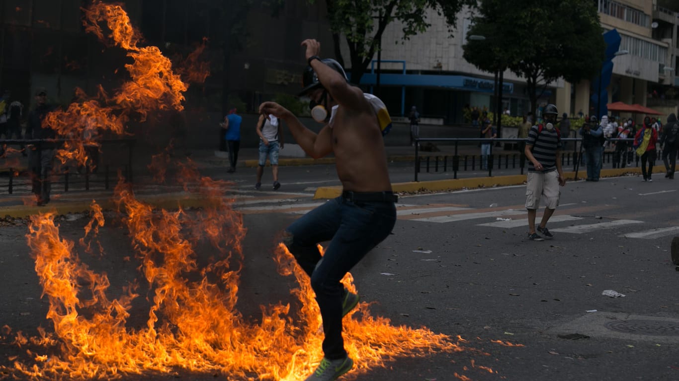 Ein Demonstrant mit Gasmaske springt über Feuer bei Zusammenstößen mit Sicherheitskräften. Das Militär steht hinter dem Maduro-Regime.