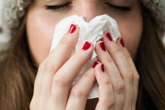 Eine Frau hält sich ein Papiertaschentuch vor das Gesicht: Die Grippewelle rollt wieder durch Deutschland.