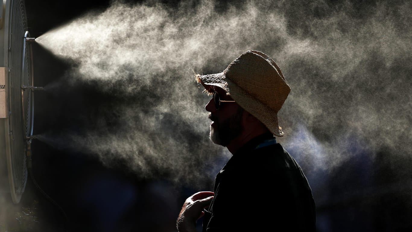 Abkühlung dringend gebraucht: Ein Tennisfan steht bei den Australian Open vor einem Ventilator, der Wassertropfen verteilt.