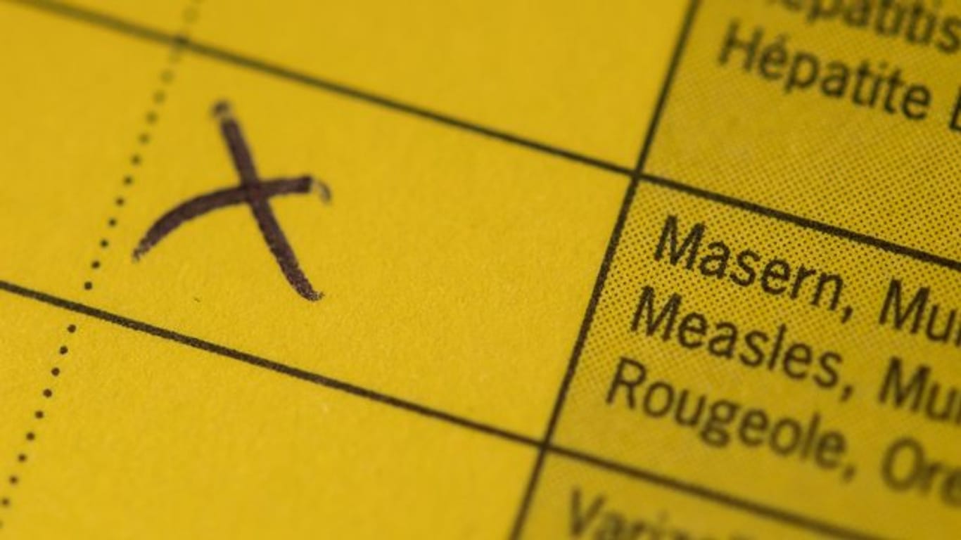 Ein Kreuz steht auf einem Impfpass, in dem eine Kombiimpfung für Masern, Mumps und Röteln eingetragen ist.