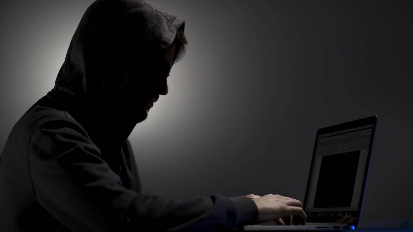 Mann mit Kapuze an einem Laptop (Symbolbild): Bei dem Verdächtigen beschlagnahmten die Beamten mehrere Computer und Datenträger.
