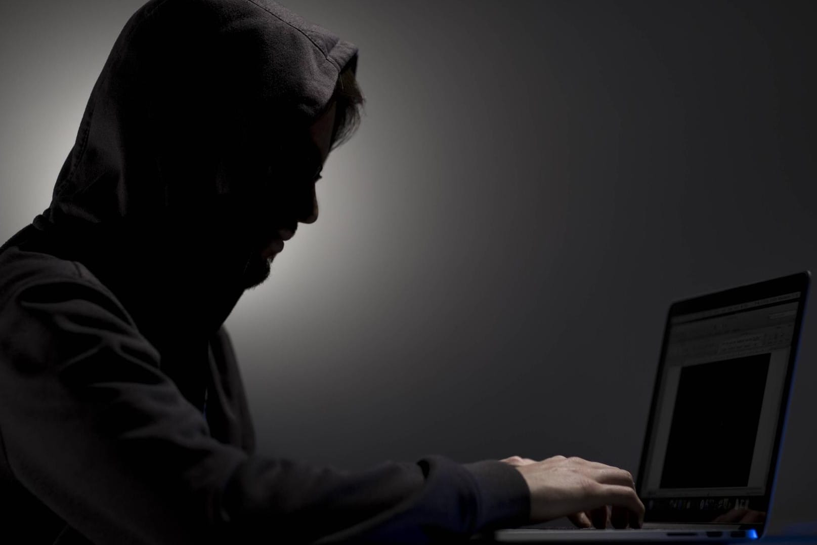 Mann mit Kapuze an einem Laptop (Symbolbild): Bei dem Verdächtigen beschlagnahmten die Beamten mehrere Computer und Datenträger.