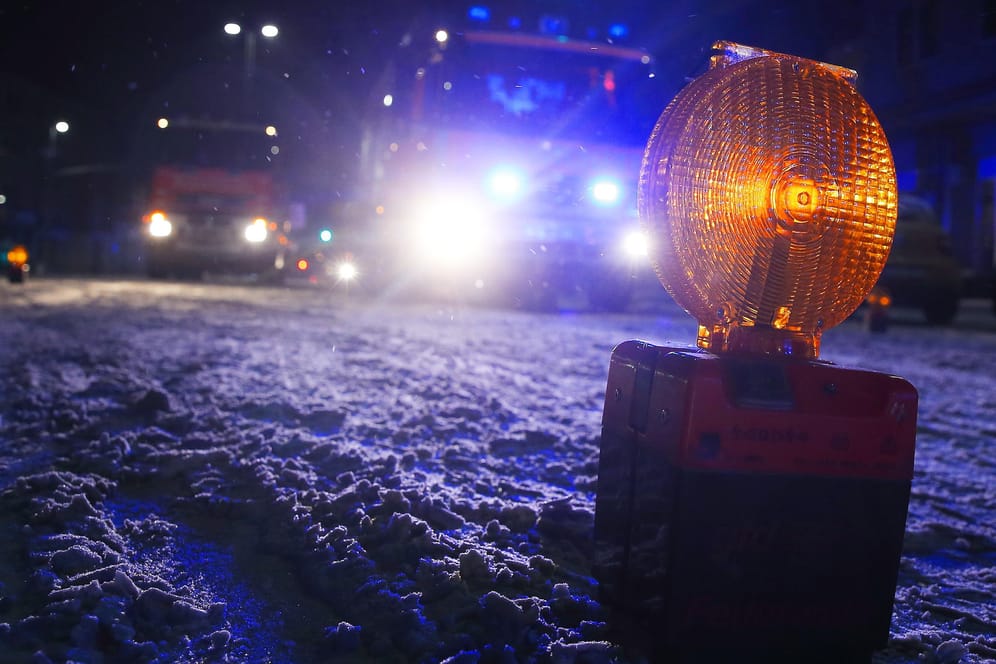Warnleuchten der Feuerwehr stehen auf einer schneebedeckten Straße in NRW. Schnee und Glätte haben zu tödlichen Unfällen geführt.