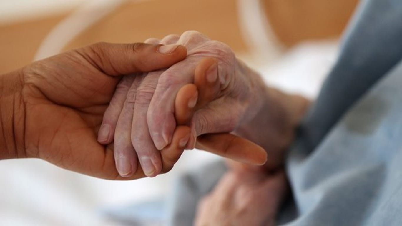 Eine Pflegerin hält im Altenheim die Hand einer Bewohnerin.