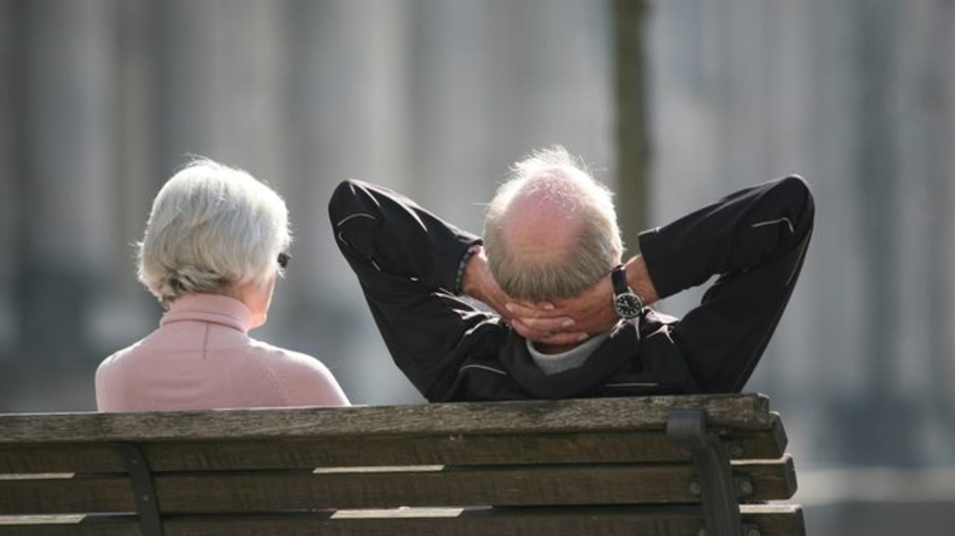 Ein Rentnerpaar sitzt auf einer Bank vor dem Reichstag und sonnt sich.
