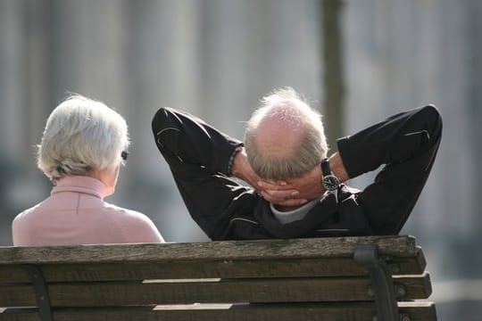 Ein Rentnerpaar sitzt auf einer Bank vor dem Reichstag und sonnt sich.