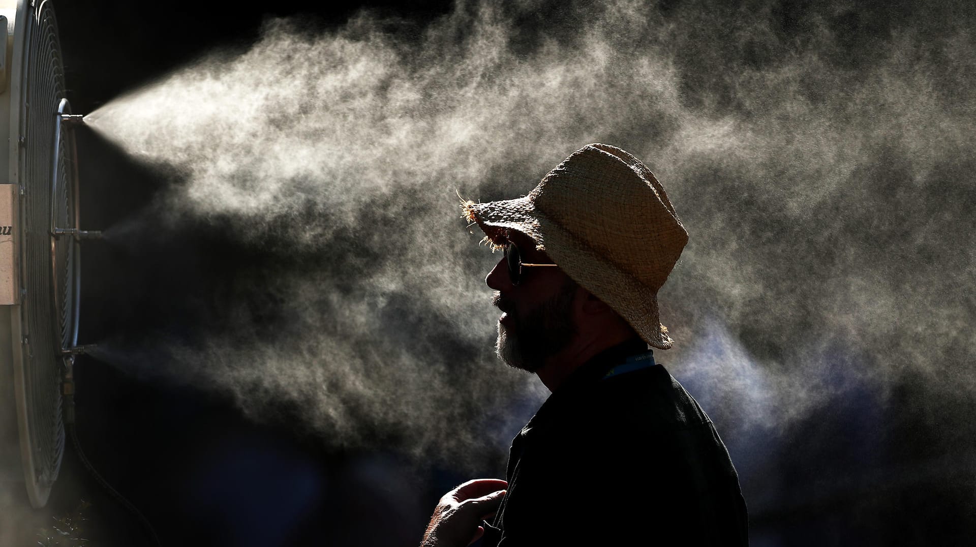 Ein Tennisfan bei den Australian Open vor einem Ventilator, der Wasser verteilt.