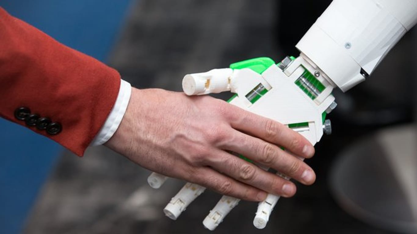 Ein humanoider Roboter gibt einem Menschen die Hand am Stand von ioX Lab bei der IT-Messe CeBIT.