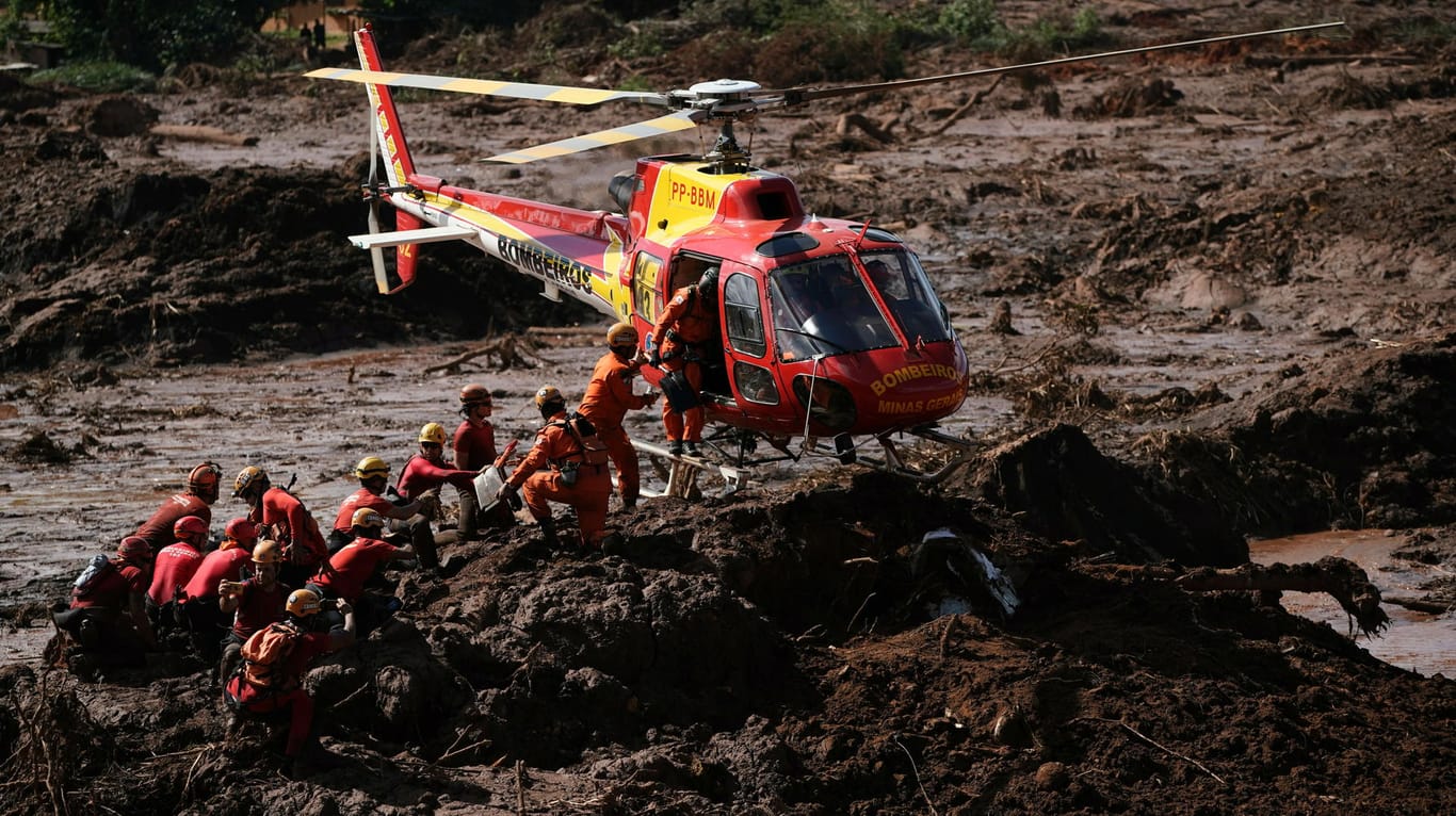 Brumadinho: Ein Hubschrauber landet neben Feuerwehrleuten, die nach Opfern im Schlamm nach einem Dammbruch an einer Mine suchen.