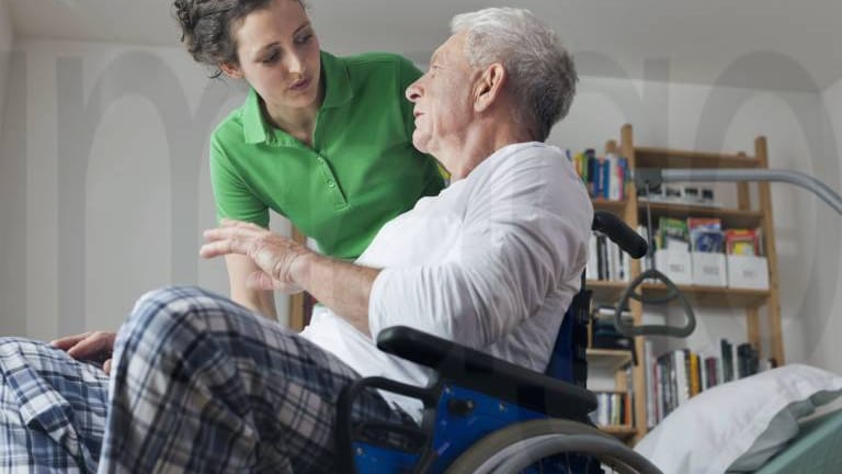 Älterer Mann im Rollstuhl mit Pflegerin