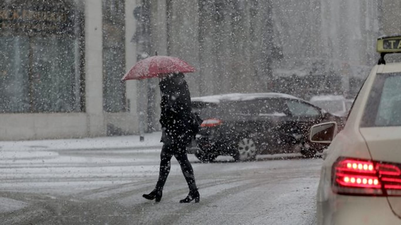 Ein Frau mit Schirm geht im Schneetreiben über eine Straße in Köln.