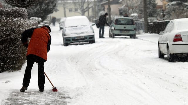 Mann räumt Gehweg frei: Wie sieht es bei der Räumpflicht für Parkplätze aus?