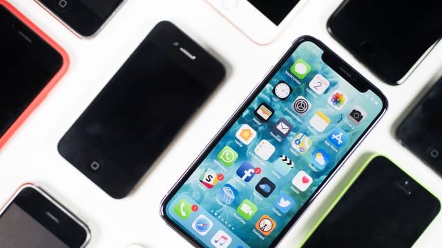Ein iPhone X liegt neben iPhones anderer Generationen auf einem Tisch. Ein iPhone X liegt neben iPhones anderer Generationen auf einem Tisch.