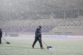 Stadionmitarbeiter versuchen das Spielfeld bei anhaltenden Schneefall zu räumen.